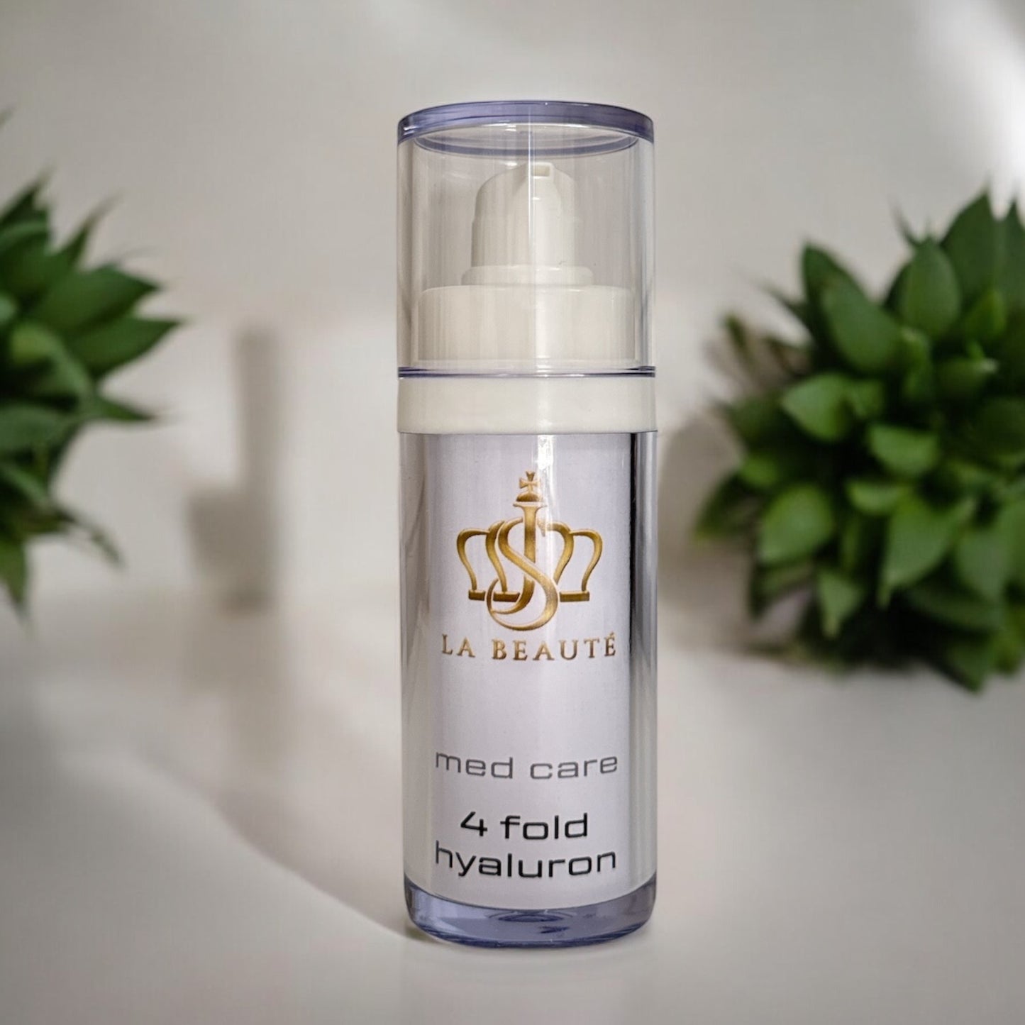 Flasche der JS La Beauté 4fold hyaluron aus der Med Care Serie mit Pumpspender – schlankes Design in Weiß mit Pflanzen im Hintergrund und goldfarbenem Logo.