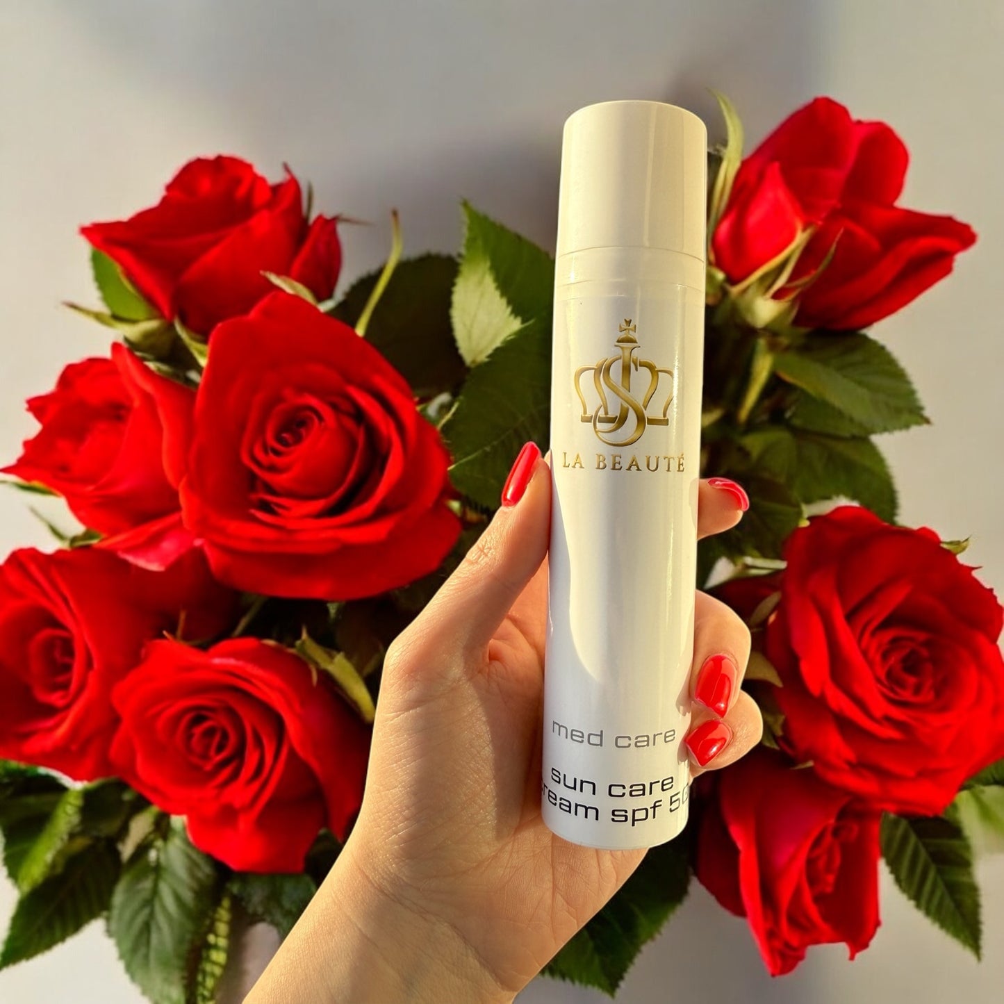 Sun Care cream SPF 50 der Serie med care von JS LA BEAUTÉ in der Hand einer Frau mit roten Rosen im Hintergrund.