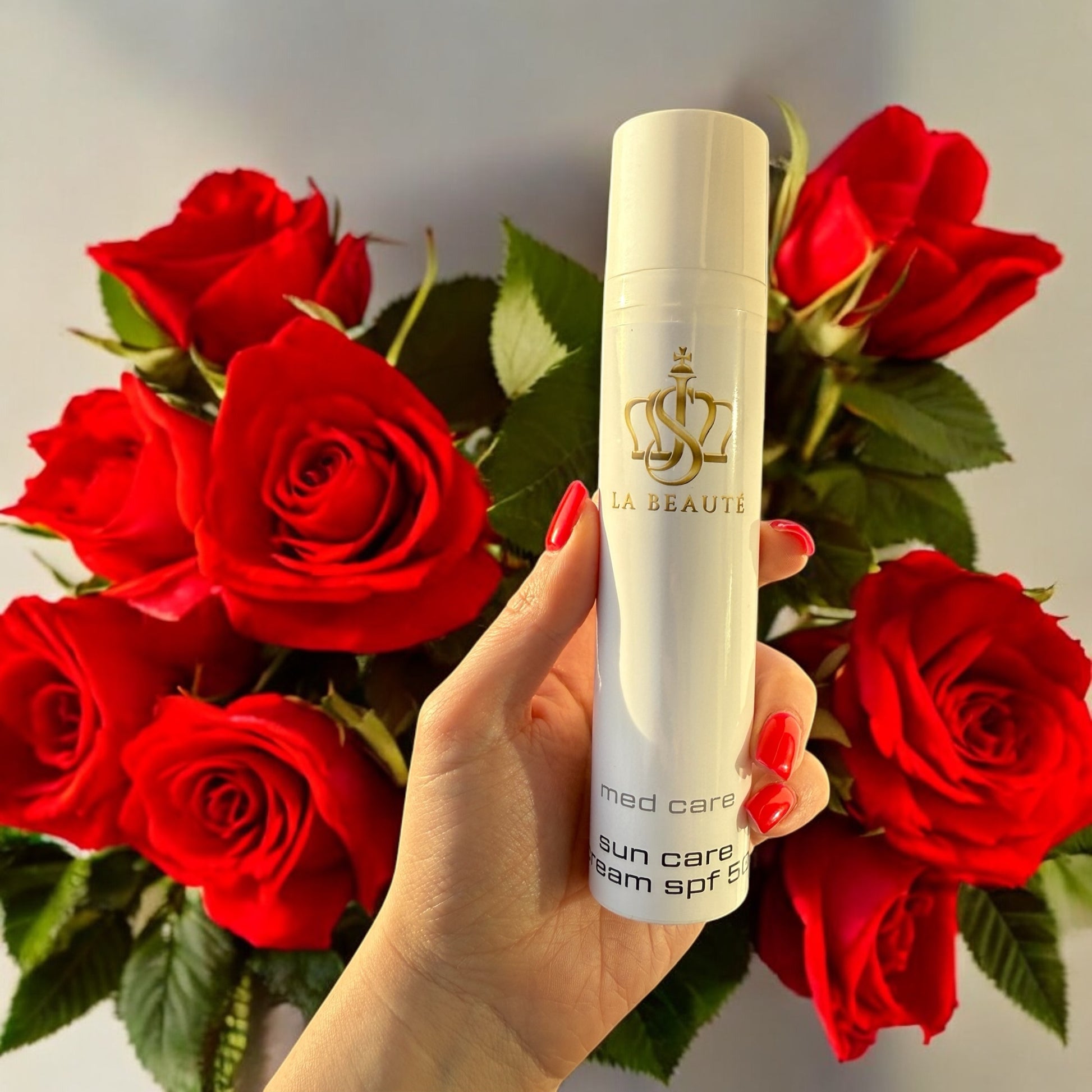 Sun Care cream SPF 50 der Serie med care von JS LA BEAUTÉ in der Hand einer Frau mit roten Rosen im Hintergrund.