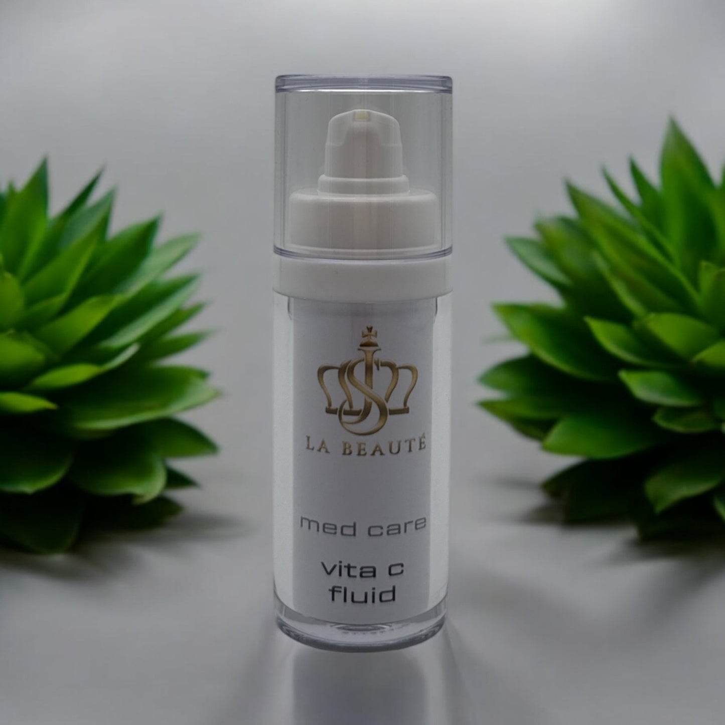 Flasche der JS La Beauté vita c fluid aus der Med Care Serie mit Pumpspender – schlankes Design in Weiß mit Pflanzen im Hintergrund und goldfarbenem Logo.