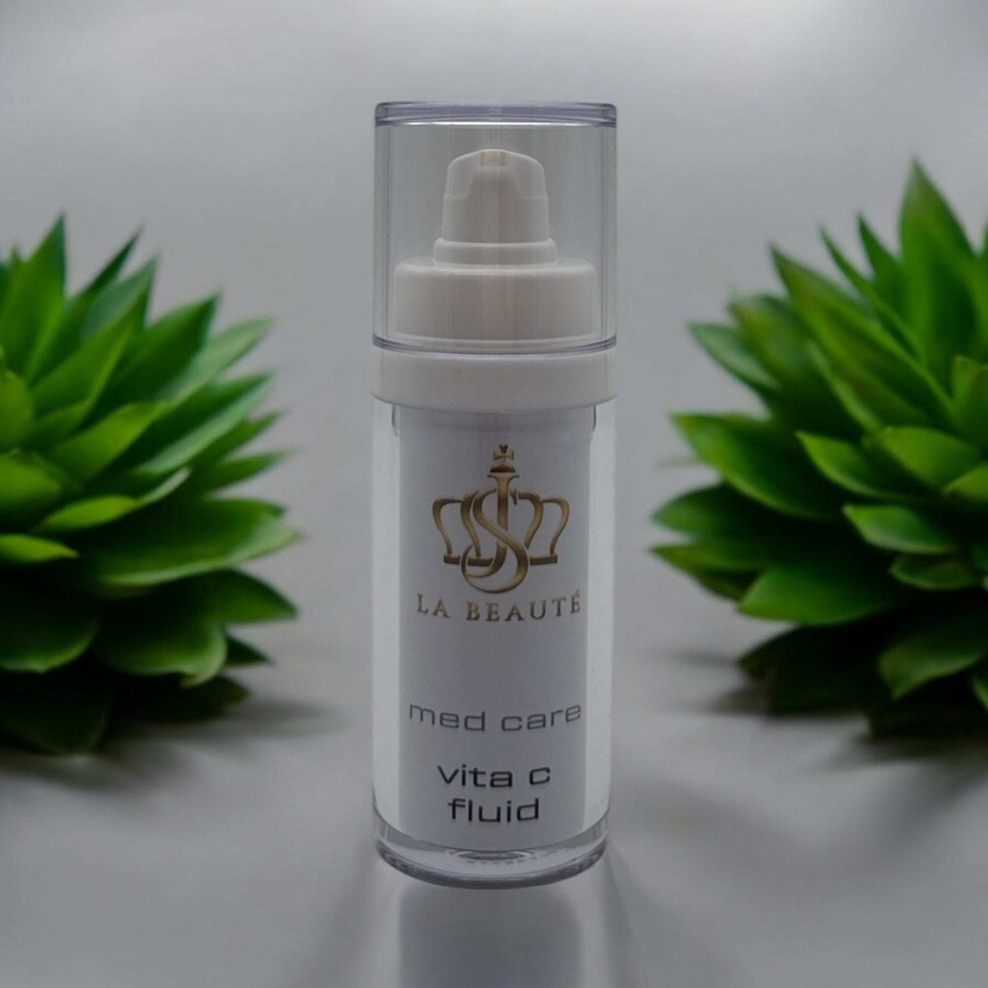 Flasche der JS La Beauté vita c fluid aus der Med Care Serie mit Pumpspender – schlankes Design in Weiß mit Pflanzen im Hintergrund und goldfarbenem Logo.