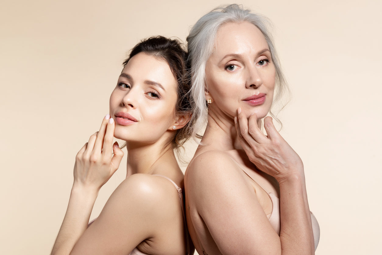 Bild von 2 Frauen im jungen und reifen Alter stehend vor einem beigenen Hintergrund.